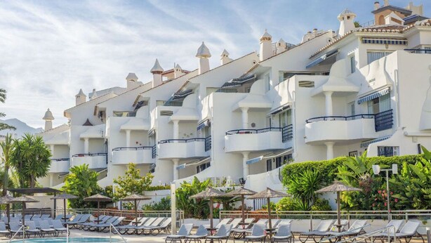 Ein Hotel mit mehreren Balkonen, einem Schwimmbad und Liegestühlen.