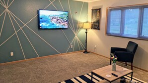 A living room with a television mounted on the wall, a floor lamp, a chair, and a coffee table. - Your cozy riverfront escape with big-city access (Council Bluffs)