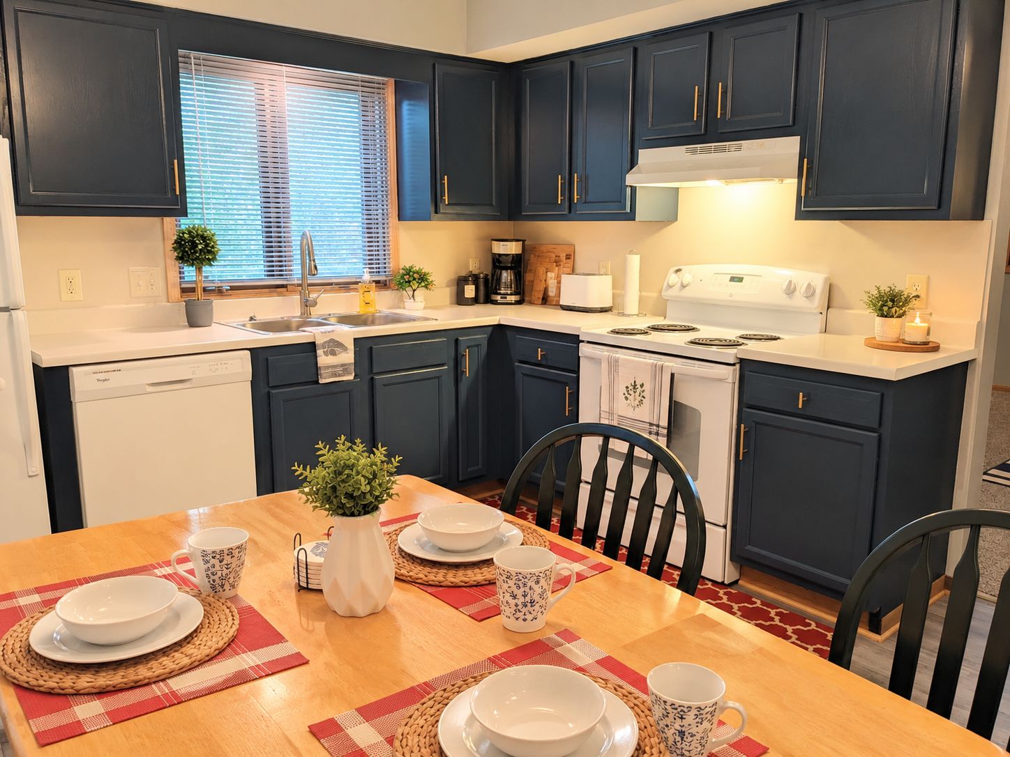 Una cocina moderna con armarios azul marino, un lavavajillas blanco, una estufa y una mesa de comedor con platos y tazas.