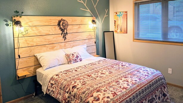 A bedroom with a wooden headboard, a patterned bedspread, and a wall-mounted dreamcatcher. - Your cozy riverfront escape with big-city access (Council Bluffs)