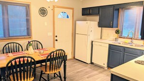 A compact kitchen with a refrigerator, dishwasher, and a dining area with a table and chairs. - Your cozy riverfront escape with big-city access (Council Bluffs)