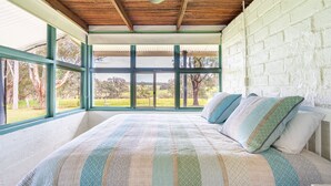 Een slaapkamer met een groot bed, uitzicht op het landschap door grote ramen, en een witte bakstenen muur.