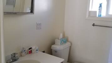 A bathroom with a white sink, mirror, and toilet. There is a window with a towel rack and a bottle of air freshener.