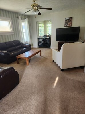 A living room with a ceiling fan, a black leather sofa, a white sofa, a wooden coffee table, and a television. - cozy Home away from home (Bridgeport)