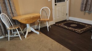 Un comedor con una mesa de madera y dos sillas blancas, un tapete estampado y una puerta con panel de vidrio.