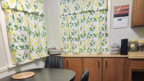 Un comedor con una mesa redonda, sillas negras, armarios de madera y una ventana con cortinas de estampado de limón.
