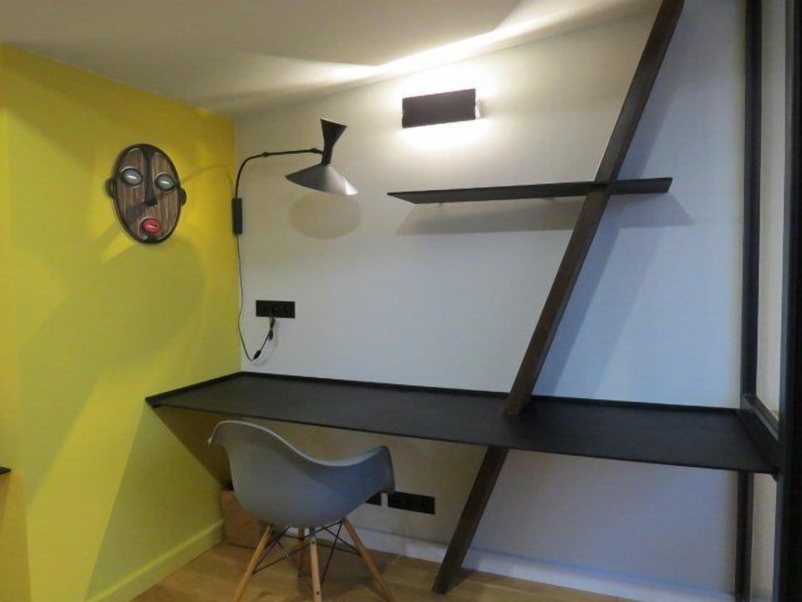 A room with a desk, a chair, and a wall-mounted shelf.