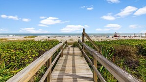 Una passerella in legno che conduce a una spiaggia, con una torretta per i bagnini in lontananza.