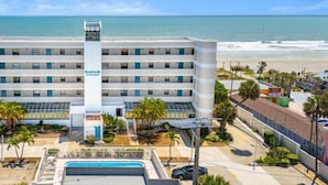 Un hotel a più piani con una torre centrale, una piscina e vista sulla spiaggia.