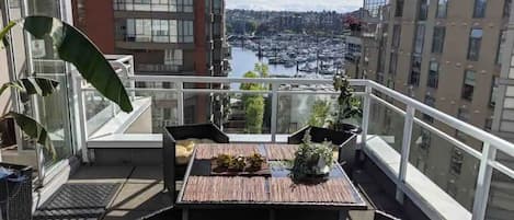 A balcony with a table and chairs, a potted plant, and a view of a marina and cityscape.