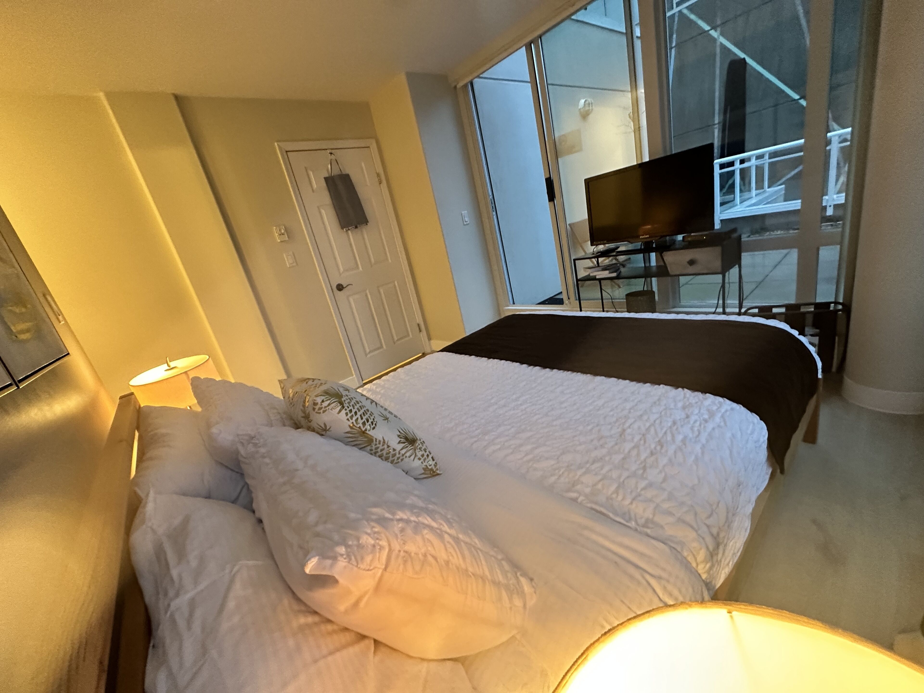 A hotel room with a bed, a TV on a desk, and a window with a view of a building.