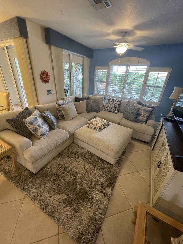A living room with a sectional sofa, a rug, and a ceiling fan.