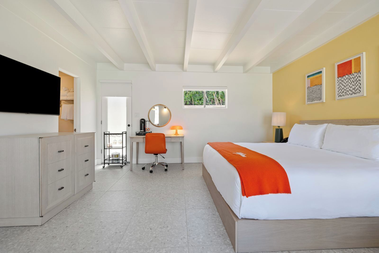 A hotel room with a bed, a desk with a chair, a TV, and a window with a view of greenery.