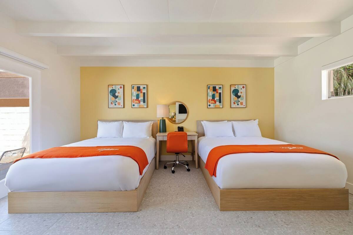 A hotel room with two beds, a desk, a chair, and artwork on the walls.