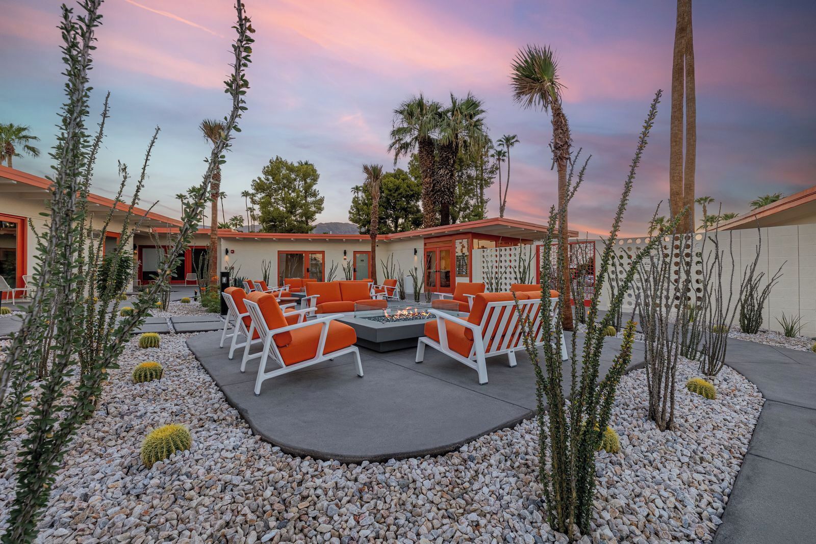 An outdoor seating area with white and orange chairs, a fire pit, and cacti.