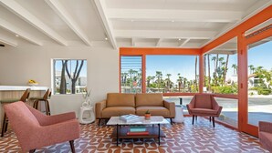 A modern living room with a sofa, two armchairs, a coffee table, and a dining area with a bar stool and a bowl of fruit. - Mojave Resort - Adults Only (Palm Desert)