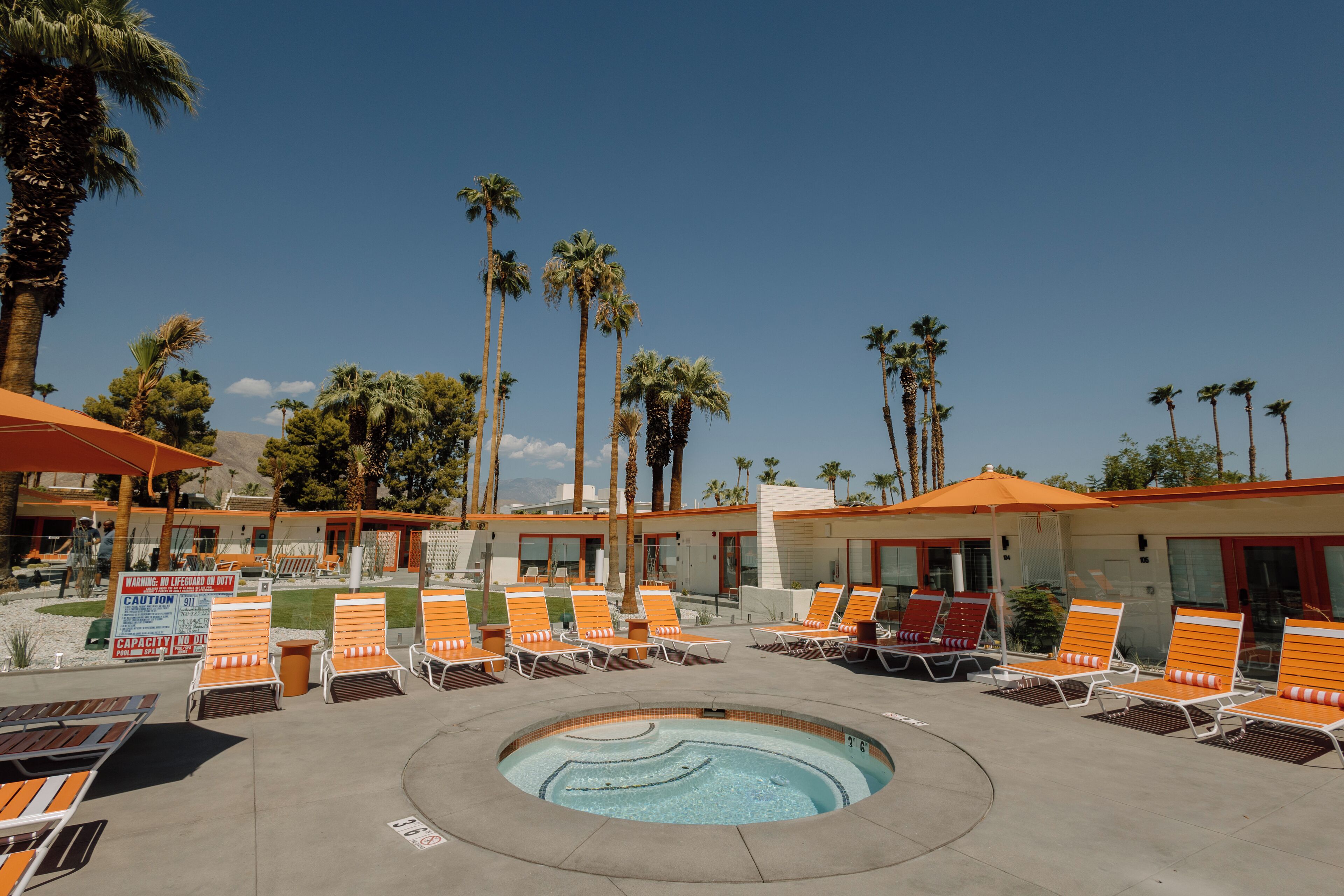 Un área de piscina con sillones de descanso y palmeras.