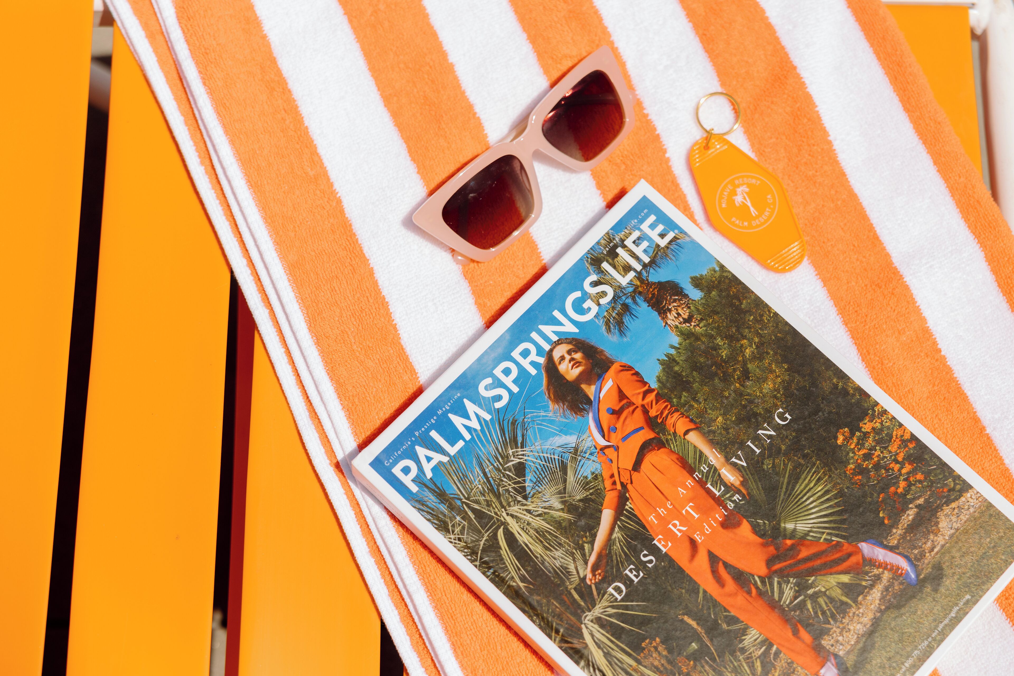 Una revista titulada 'Palm Springs Life' con una imagen tropical, gafas de sol y un llavero sobre una toalla a rayas.