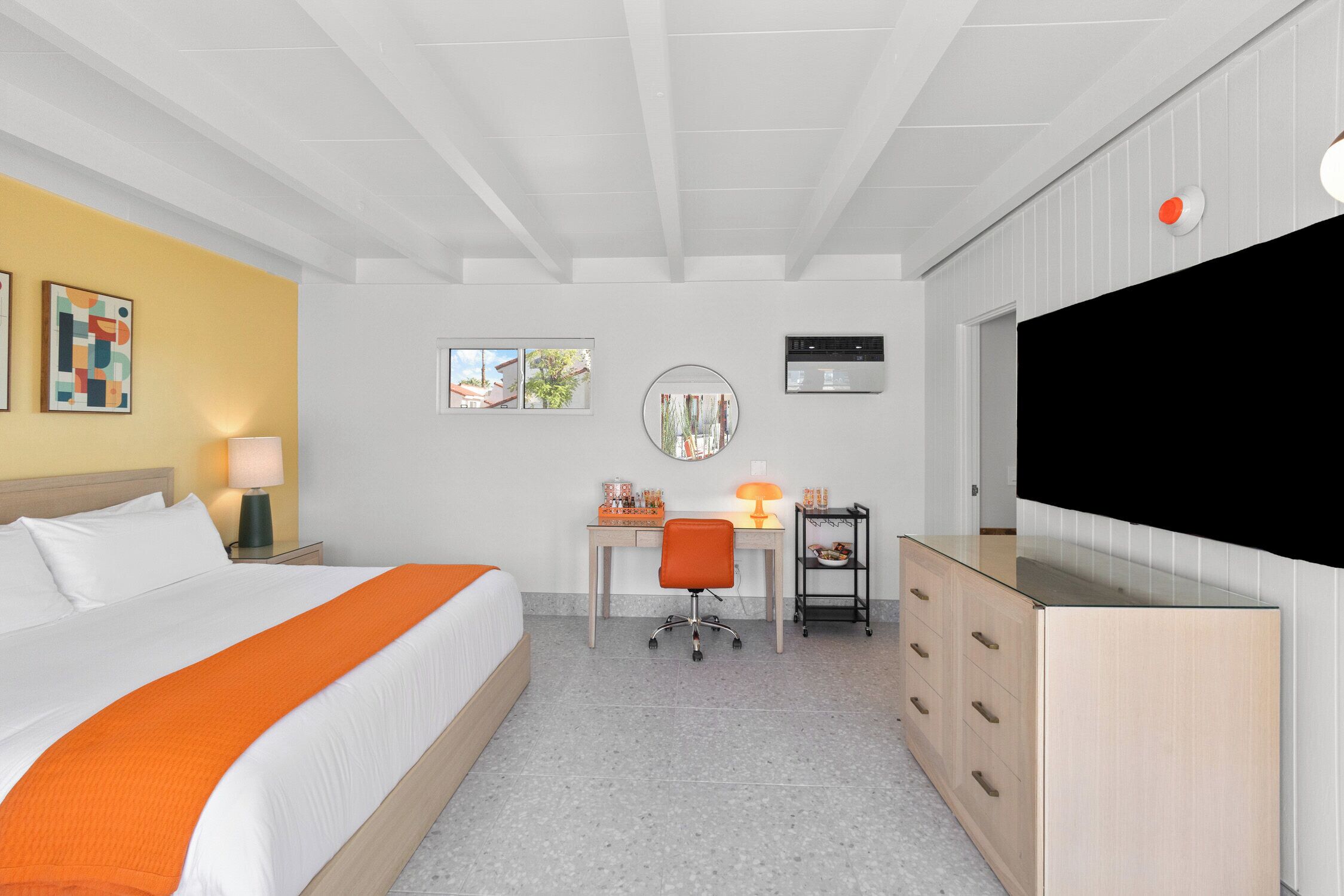 Una habitación de hotel con cama, escritorio, silla, televisor y un mueble bajo.