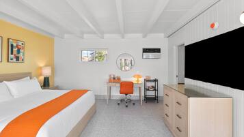 Una habitación de hotel con cama, escritorio, silla, televisor y un mueble bajo.