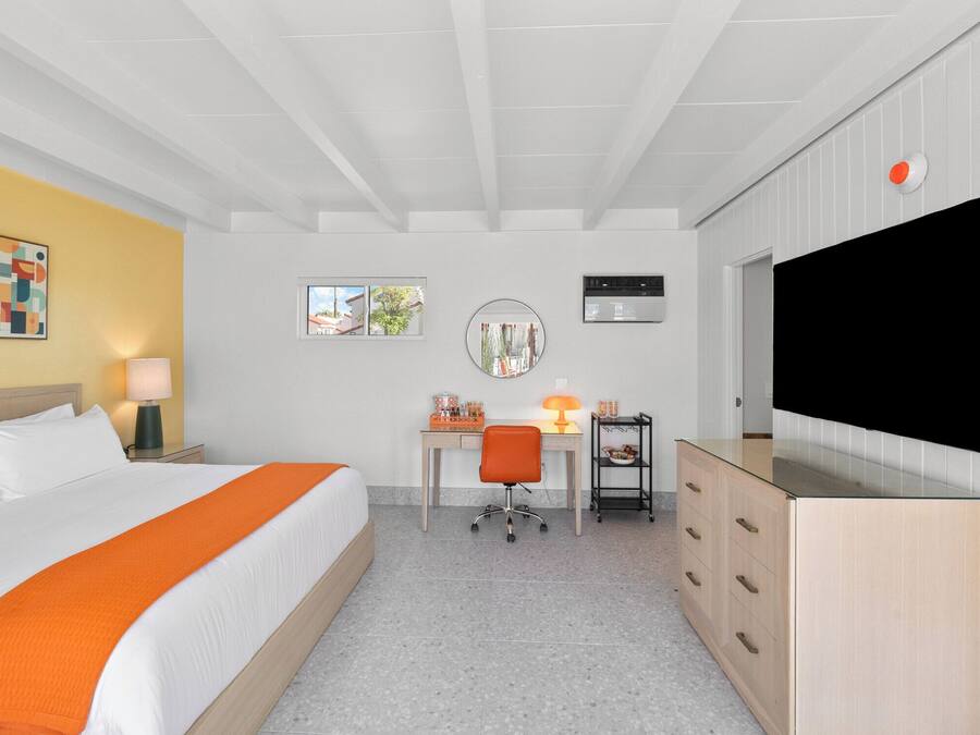Una habitación de hotel con cama, escritorio, silla, televisor y un mueble bajo.