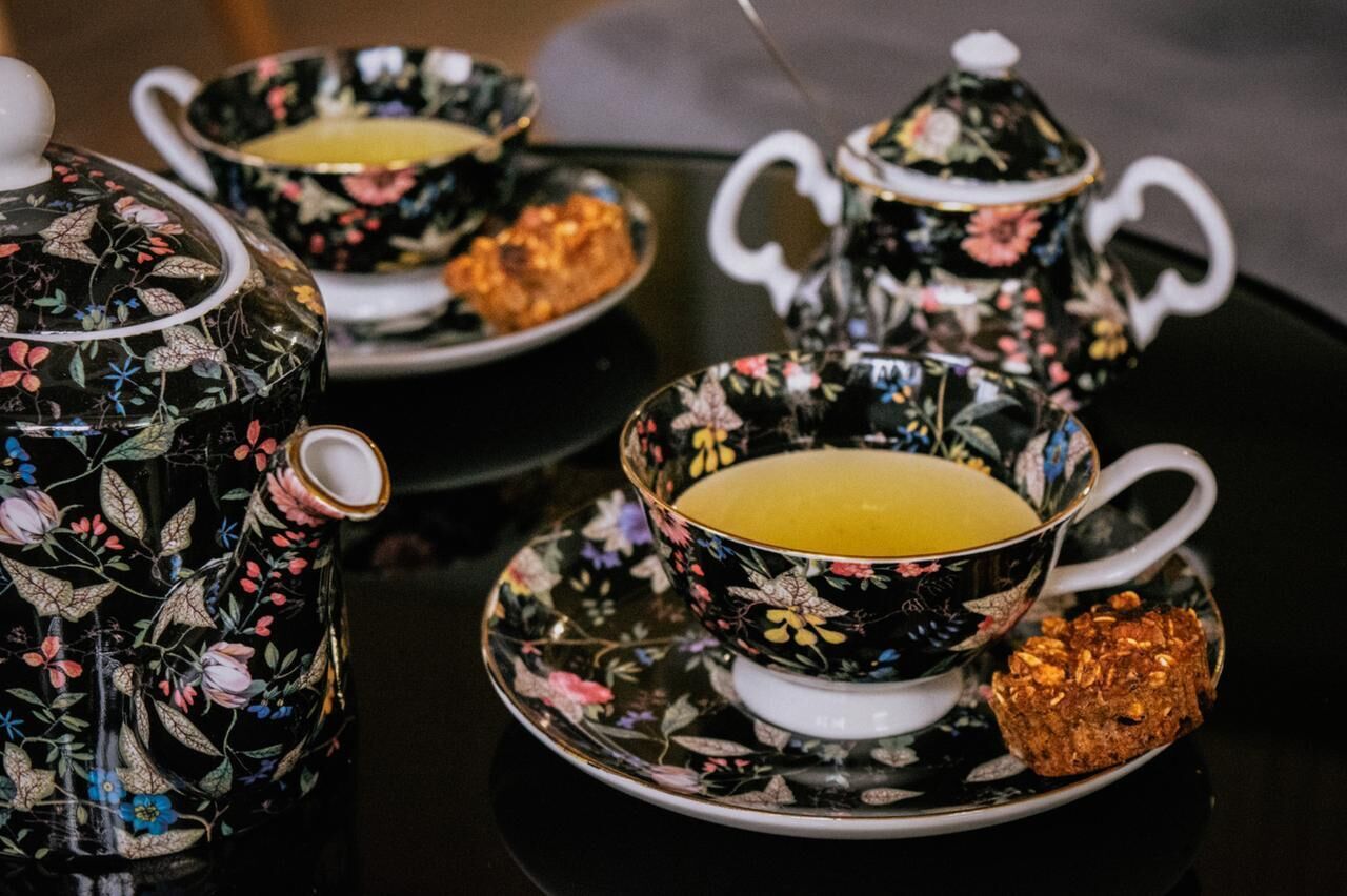 Un service à thé orné de motifs floraux, posé sur une table noire et blanche.