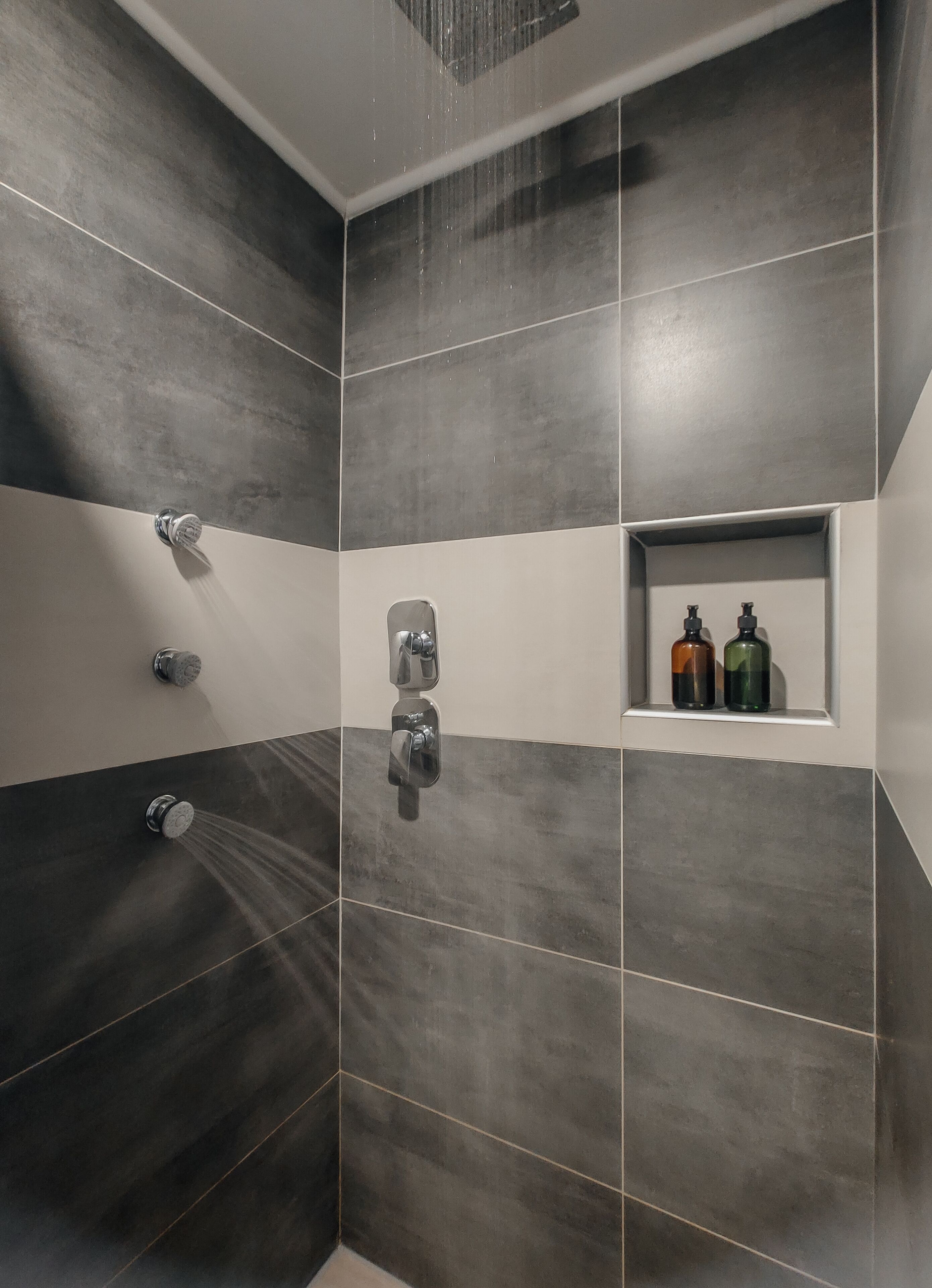 Una doccia con diversi rubinetti e uno scaffale con articoli da toilette.