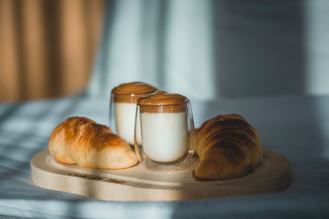 Two croissants and two glass jars of milk on a wooden tray.