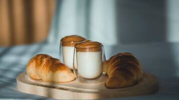 Two croissants and two glass jars of milk on a wooden tray.