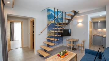 Una sala de estar moderna con una escalera de madera, un comedor con un frutero y una cocina al fondo.
