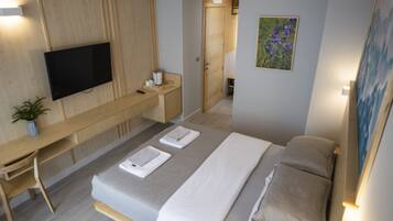 A modern hotel room with a bed, a desk, a flat-screen TV, and a painting on the wall.