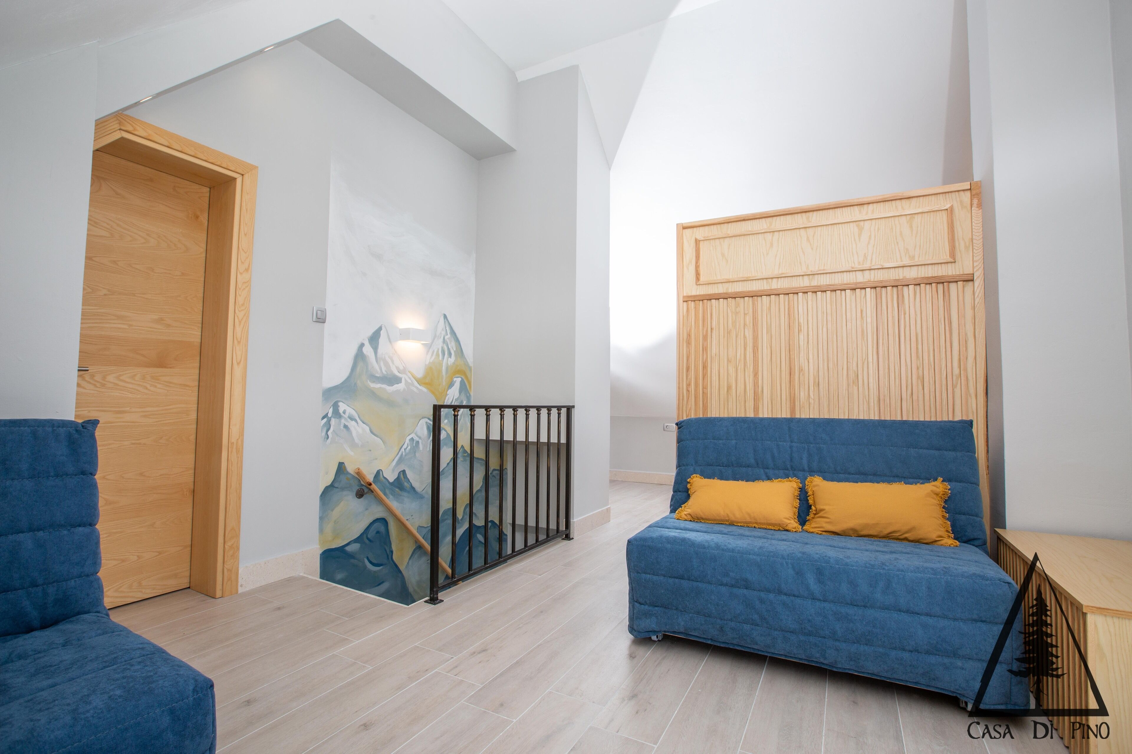 Une pièce moderne avec un canapé bleu, une porte en bois et un tableau représentant une montagne accroché au mur.
