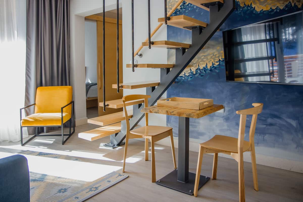 Un intérieur moderne avec un escalier, des chaises en bois, une table et une grande fenêtre.