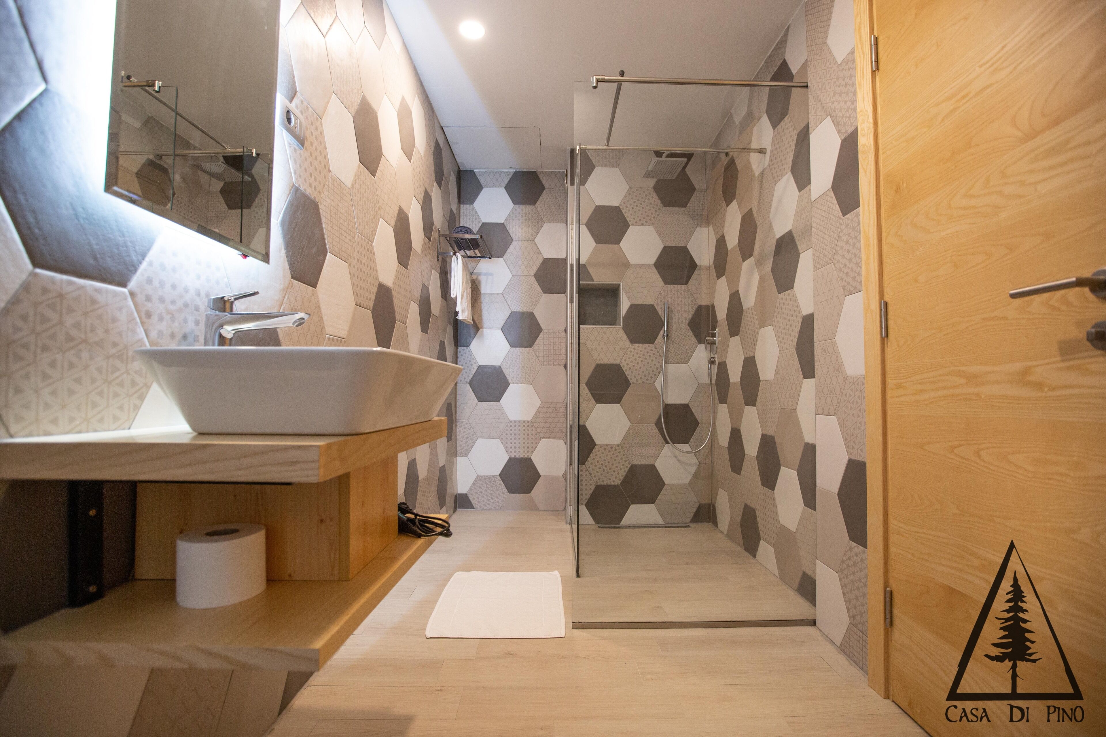 Une salle de bain moderne avec un grand lavabo, une douche en verre et une porte en bois ornée d’un logo.