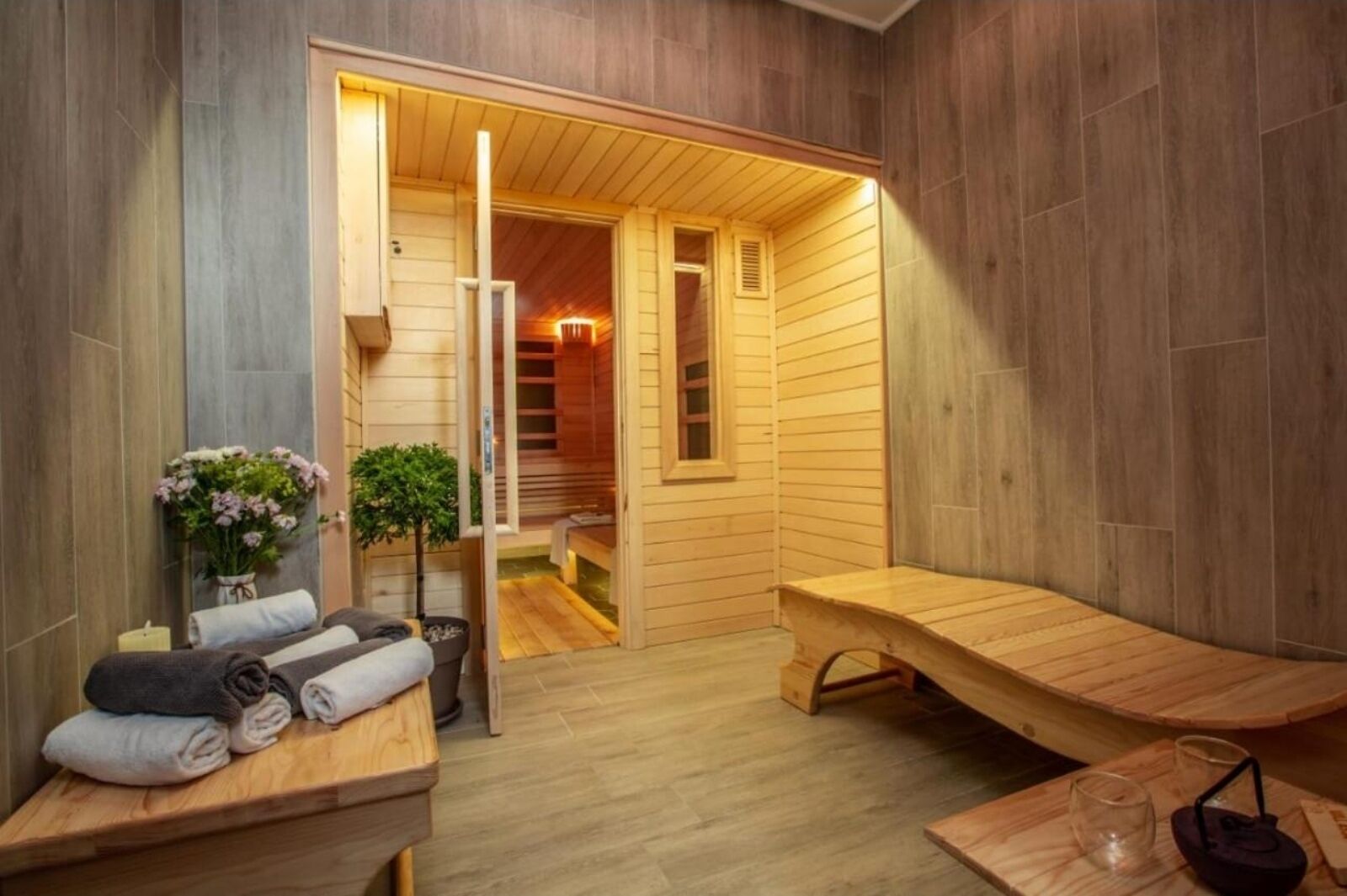 Une salle de sauna en bois avec des bancs, un banc avec une serviette, une petite table avec un verre et une plante en pot.