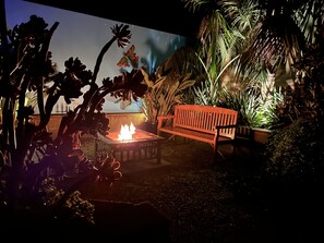 A patio area with a fire feature, a wooden bench, and various tropical plants. - Bijoux on Jetty - Cosy House/Spa/Firepit/PoolTable (Rosebud)