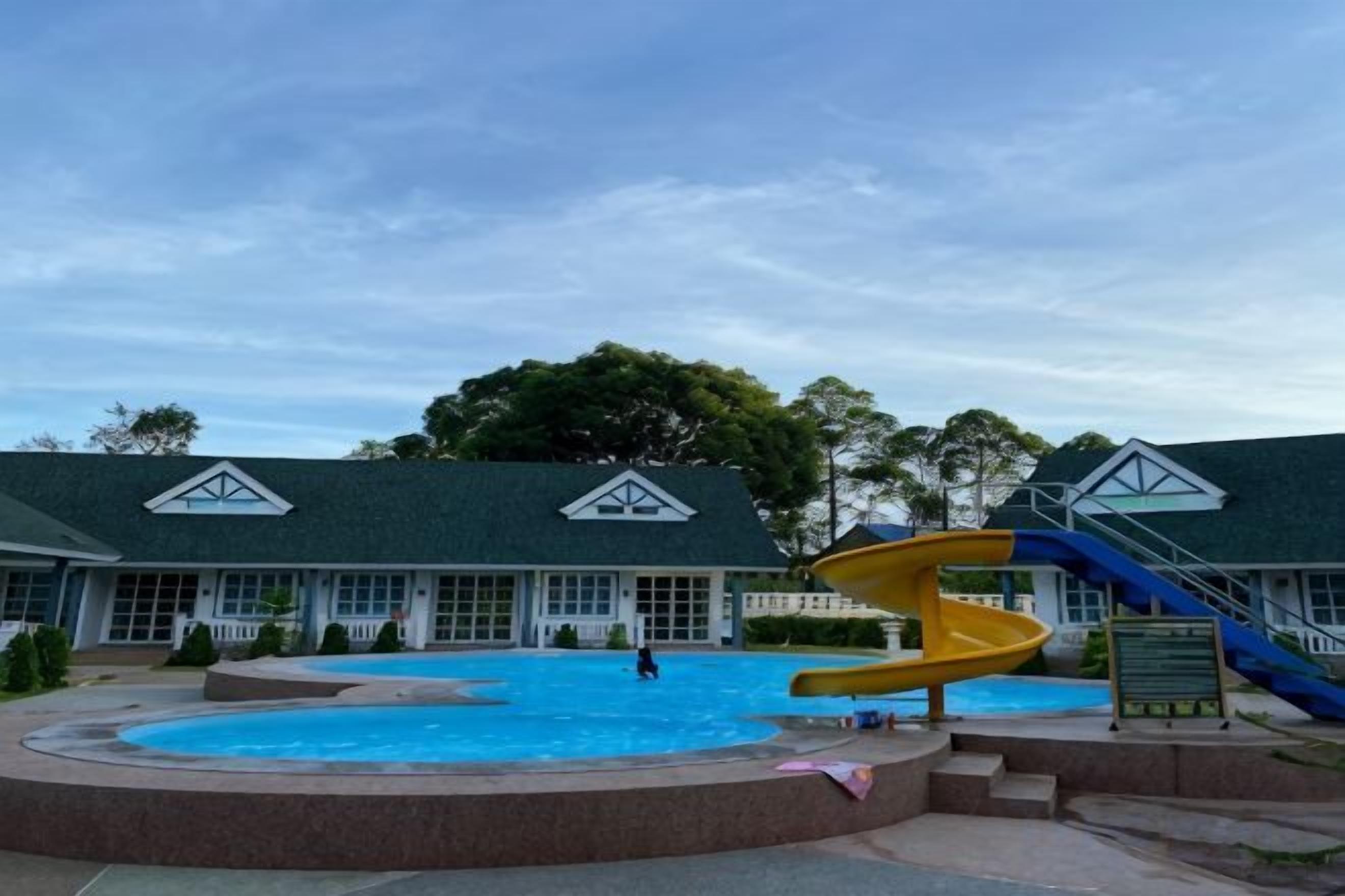 Piscina com escorregador, cercada por um edifício com telhado verde e janelas.