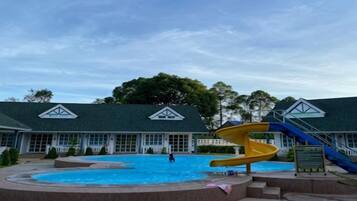 Piscina com escorregador, cercada por um edifício com telhado verde e janelas.
