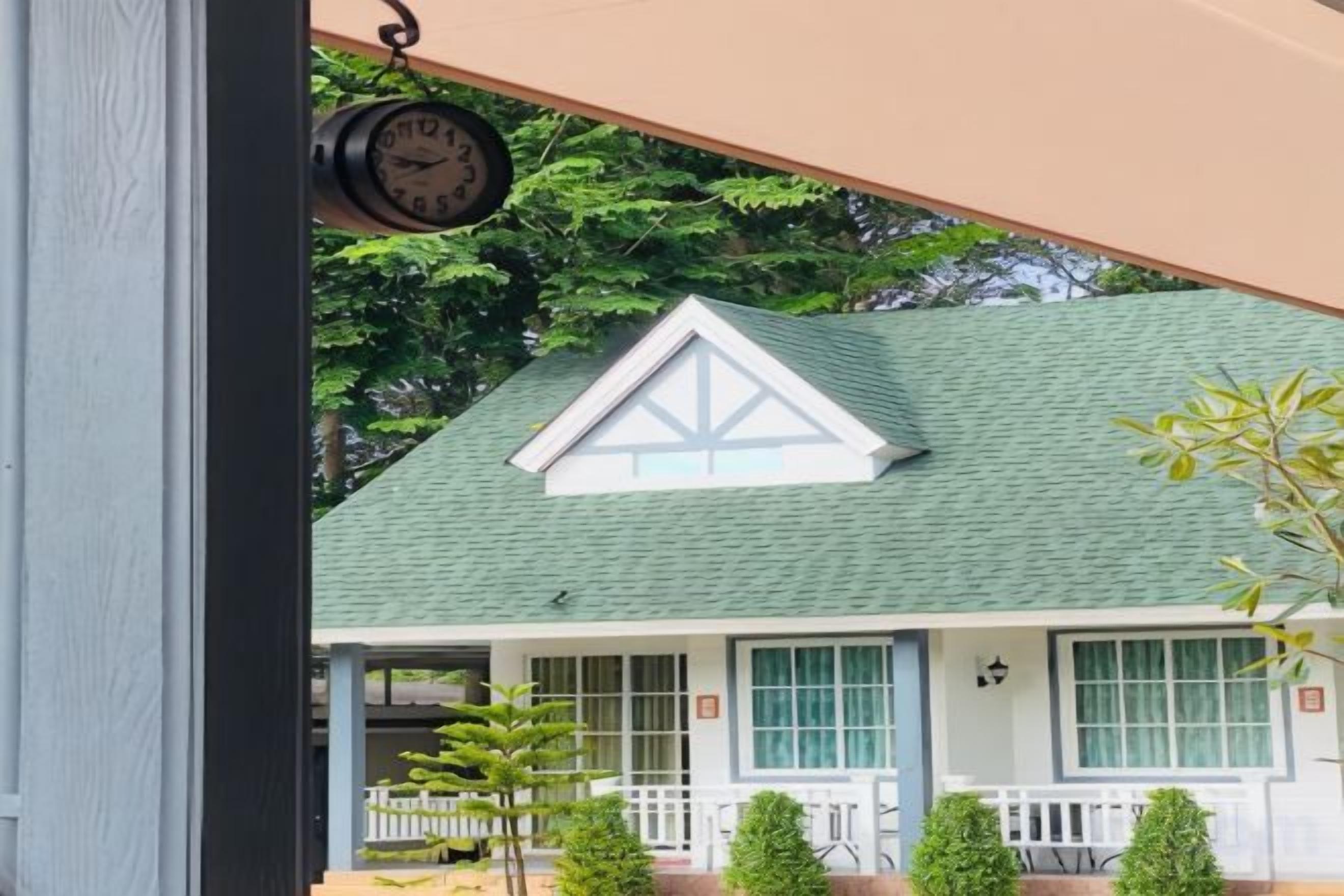 A building with a green roof, white trim, and a clock hanging from the ceiling.