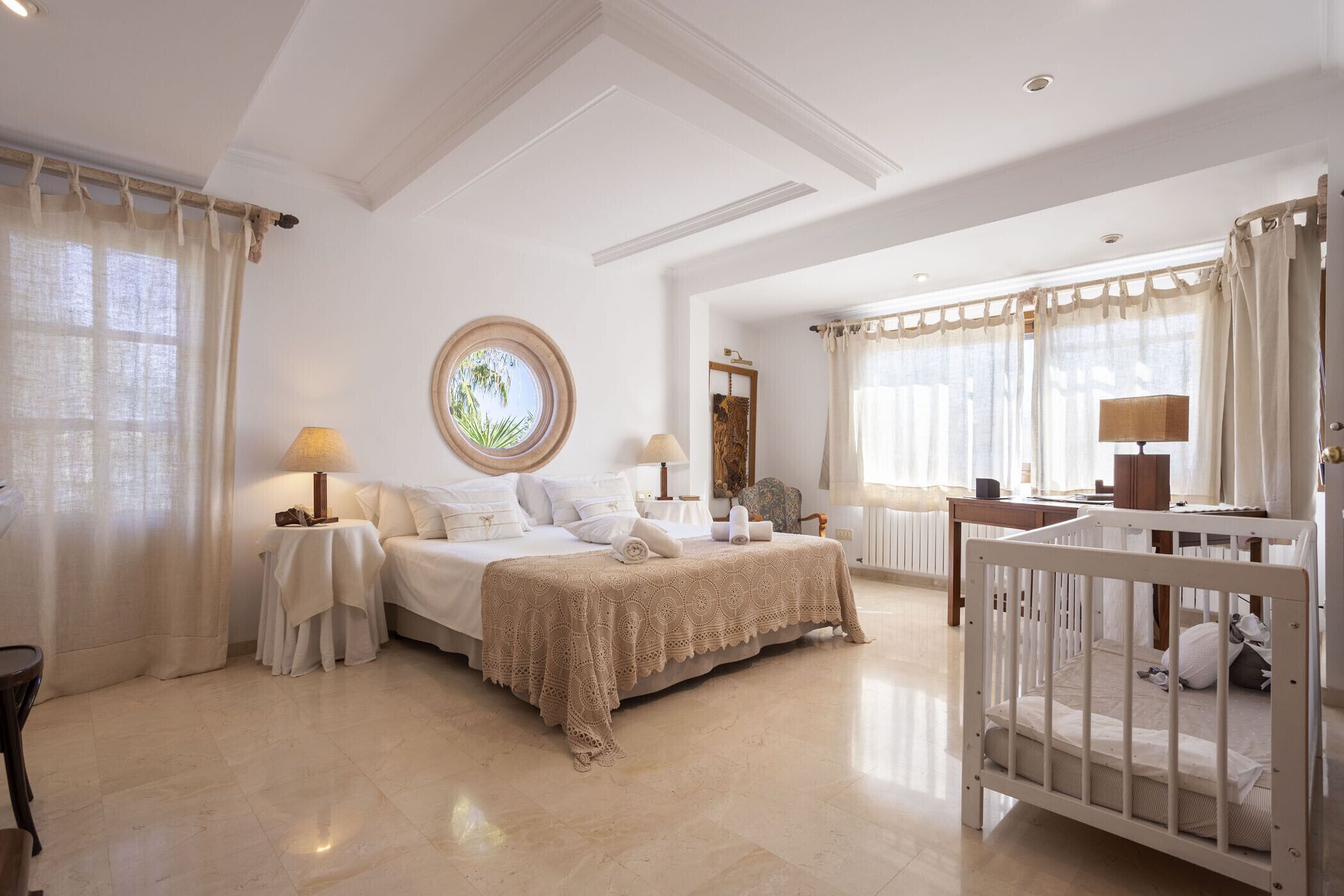 A spacious bedroom with a large bed, a crib, and a round window.