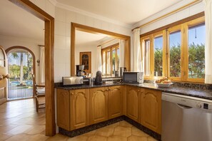 A kitchen with wooden cabinets, a Bosch dishwasher, a microwave, and a large window with curtains.