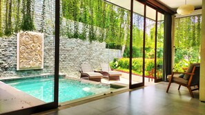 A modern outdoor pool area with a stone wall, lounge chairs, and a glass-enclosed space.