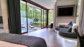 A modern bedroom with a large bed, a sofa, and a TV. There is a glass door leading to a balcony with a pool and outdoor furniture. - Rama Gaia Villa (Ubud)