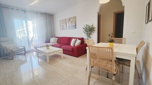 A modern living room with a red sofa, white coffee table, wicker chairs, and a dining table.