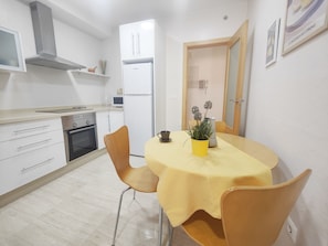 Una cocina compacta con armarios blancos, una estufa de acero inoxidable y un refrigerador blanco.