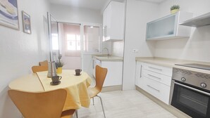 A compact kitchen with white cabinets, a stove, and a microwave. There is a dining table with chairs and a yellow tablecloth.
