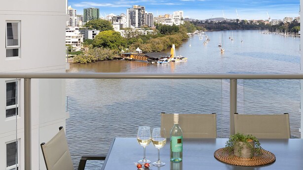 A balcony with a table set for two, overlooking a river with boats and buildings in the background. - Executive Family Suite View Parking WiFi (Brisbane)
