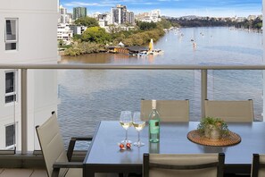 Ein Balkon mit einem Tisch für zwei Personen, mit Blick auf einen Fluss, an dessen Ufer Boote und Gebäude zu sehen sind.
