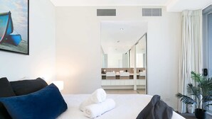 A modern hotel room with a large bed, a bedside table, a nightstand, a mirror, a window with curtains, and a potted plant. - Executive Family Suite View Parking WiFi (Brisbane)