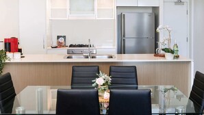A modern kitchen with a central island, stainless steel appliances, and a dining area with a glass table and black chairs. - Executive Family Suite View Parking WiFi (Brisbane)